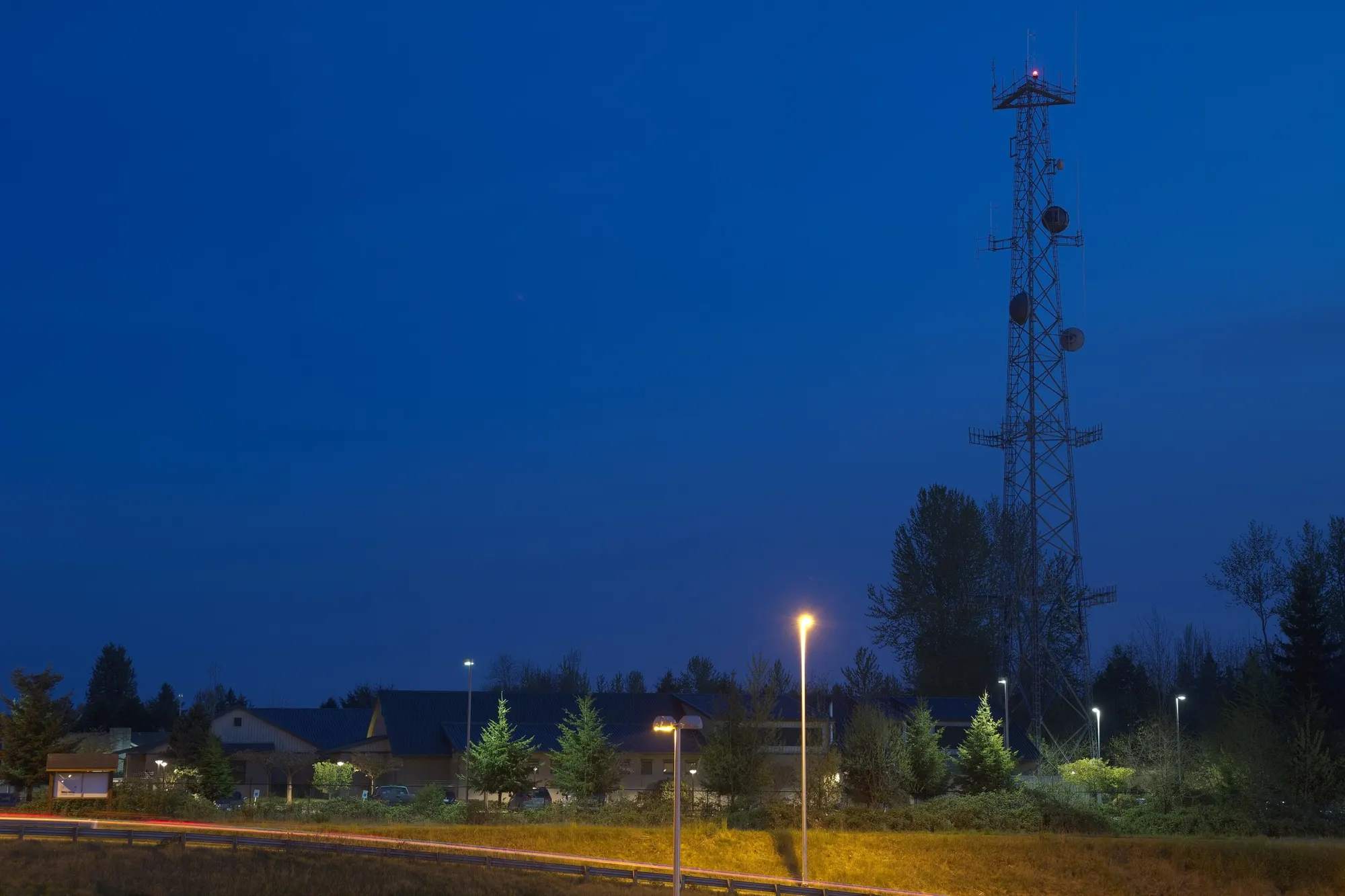 A radio tower at dusk, its lights on against a deep blue sky